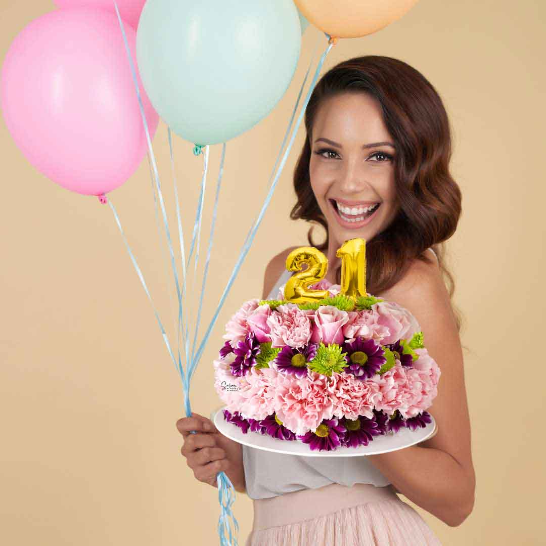 a girl holding a cake-shaped flower arrangement with balloon numbers on a white base. Salem Oregon flower delivery