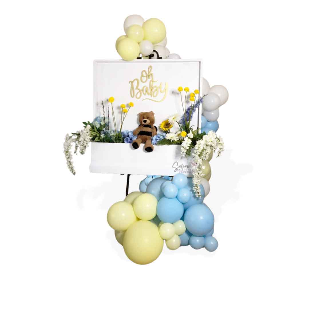 Flower Box Welcome Sign filled with blue and yellow flowers and an adorable plush sitting on a bronze easel and decorated with balloon garland. Salem Oregon balloon decor.