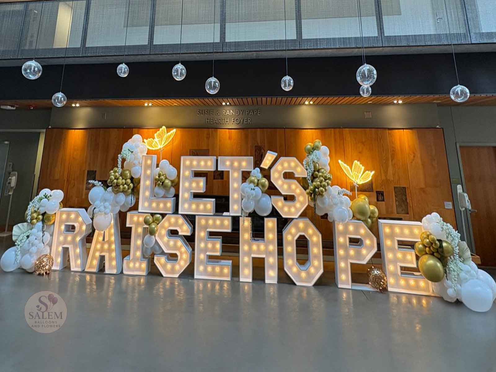 Marquee Letter display spelling LET'S RAISE HOPE decorated with balloon garlands and light up butterflies. Oregon.