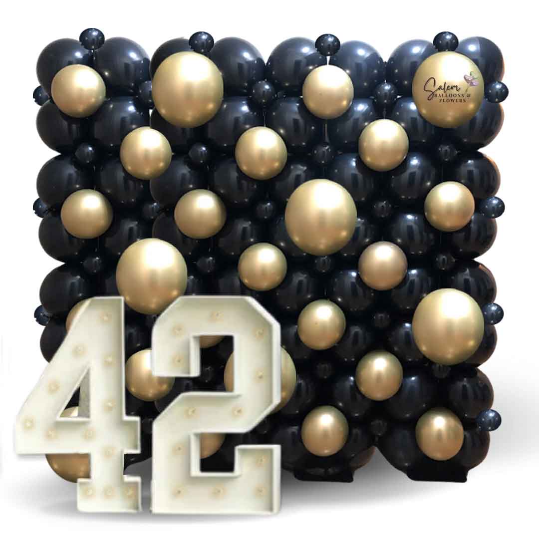 A woman posing for a picture in front of a black and gold Balloon wall with light up marquee numbers. Salem Oregon balloon decoration.