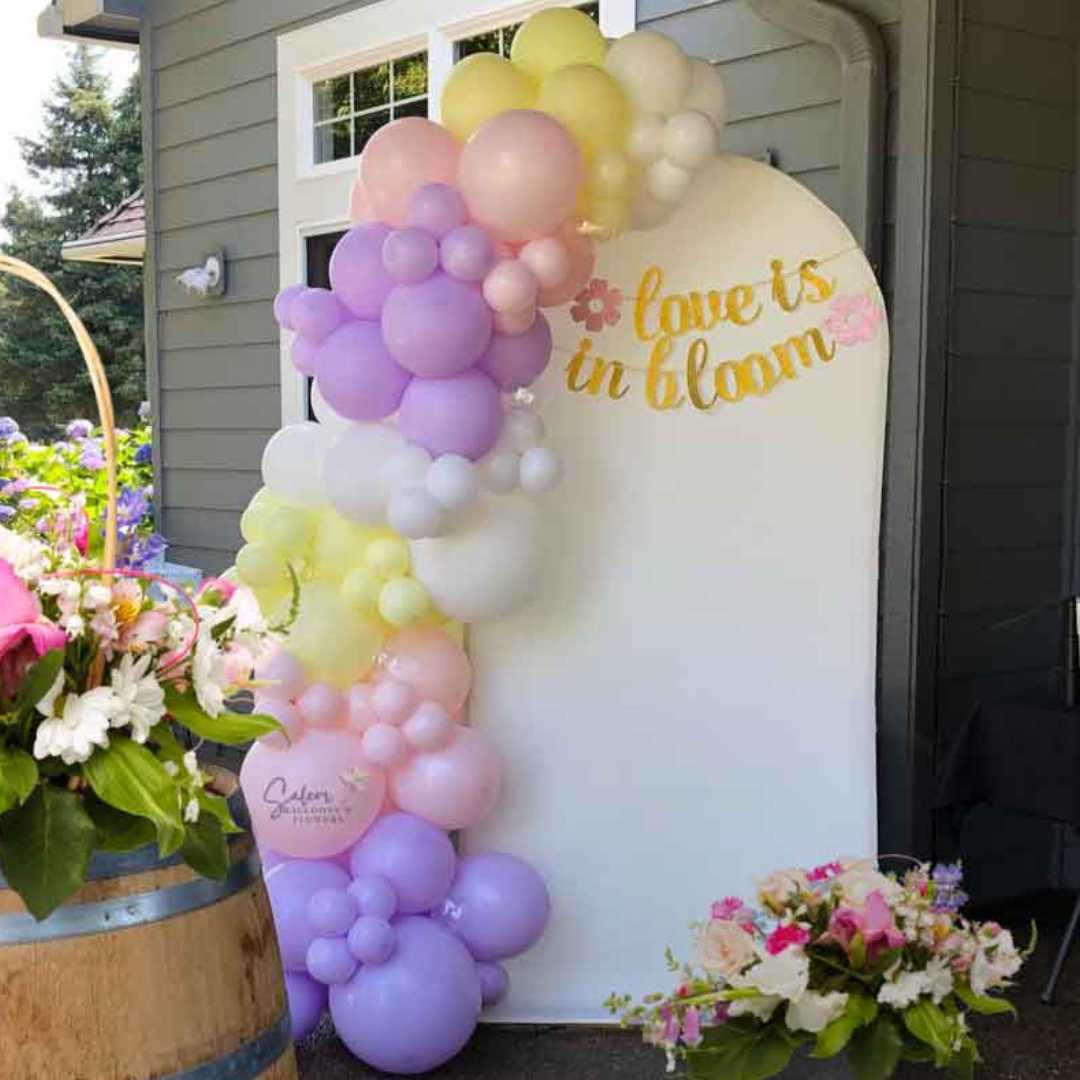 Pastel colors Balloon garland decorating an arch shaped backdrop set decorated with fresh flower arrangements. Oregon Balloon decor
