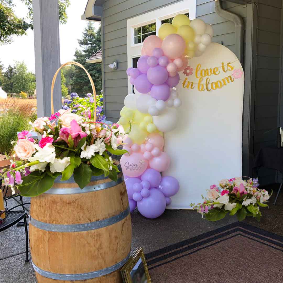 Pastel colors Balloon garland decorating an arch shaped backdrop set decorated with fresh flower arrangements on a barrel. Oregon 