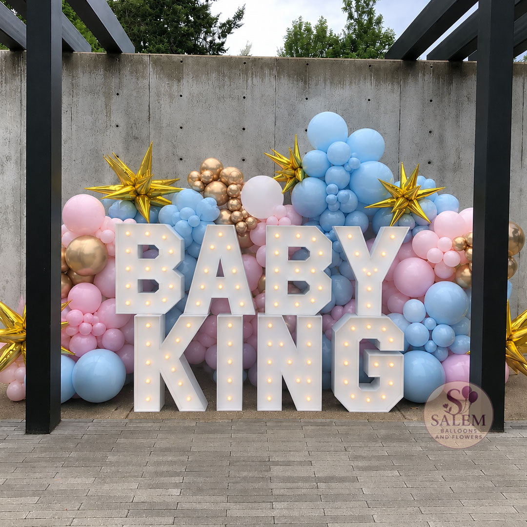 Decorative setup with pink, blue, and  gold balloons and 'BABY KING' marquee letters display against a concrete wall. Baby shower and gender reveal decor. Oregon.

