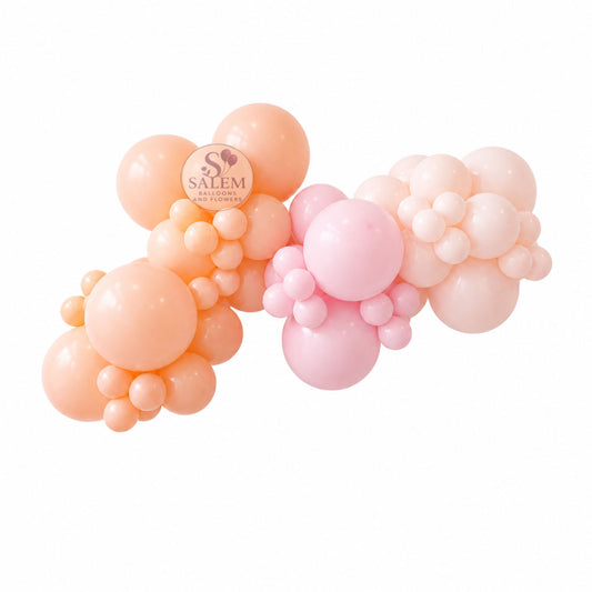 A balloon garland decoration made of clustered latex balloons in soft peach, orange, and light pink tones, shown on a plain white background by Salem Balloons and Flowers.