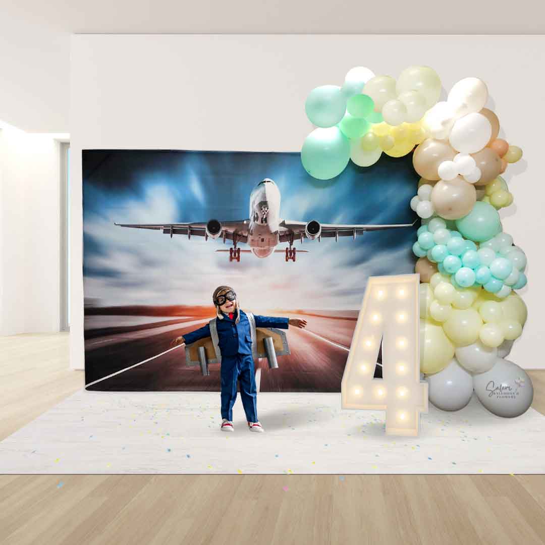 kid with a pilot uniform standing in front of a Balloon garland in pastel colors on a airplane backdrop. Salem Oregon balloon decor.