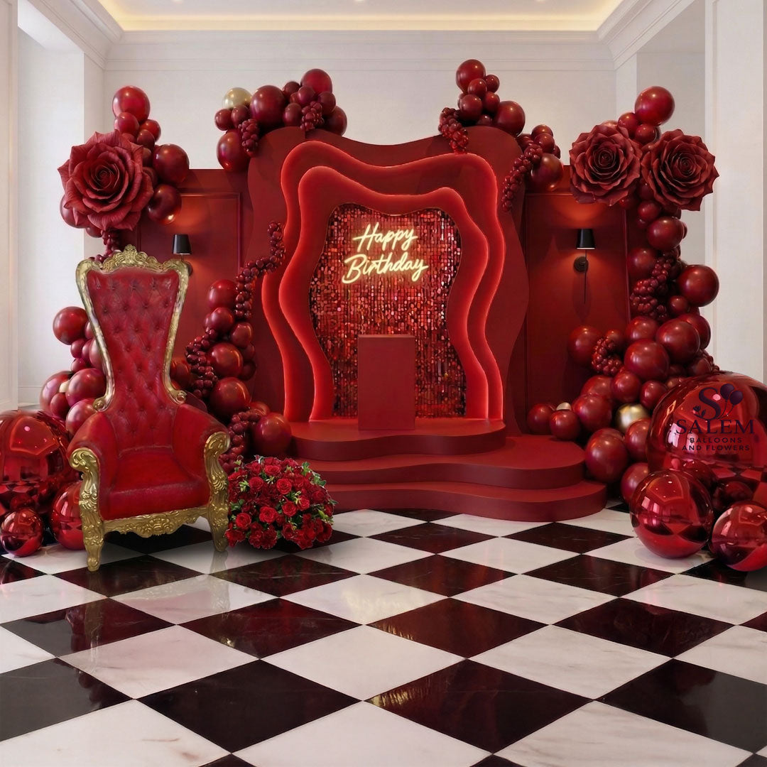 Red luxury throne themed decoration set, with balloons garlands, giant chrome sphere clusters, giant red roses, 1 wavy arch and 2 side rectangular panels with sconces and 'Happy Birthday' sign on a checkered floor room. Balloon decor made by Salem Balloons and Flowers serving Salem to portland Oregon and nearby cities.