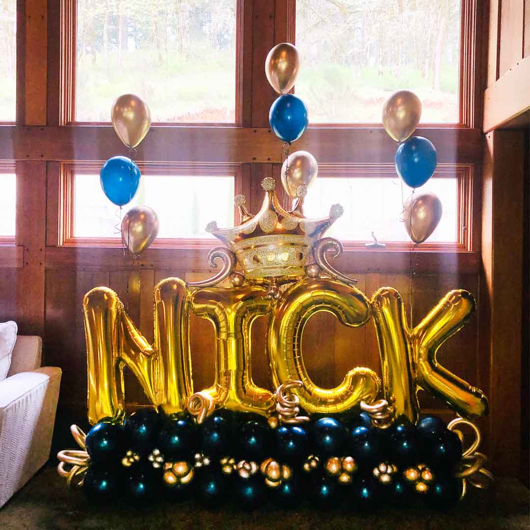 Extra large letter balloon bouquet. in navy blue, gold balloon letters with a golden crown and 3 sets of 3 helium balloons in a Living Room. Spelling the name NICK. Salem Oregon balloon decorations 