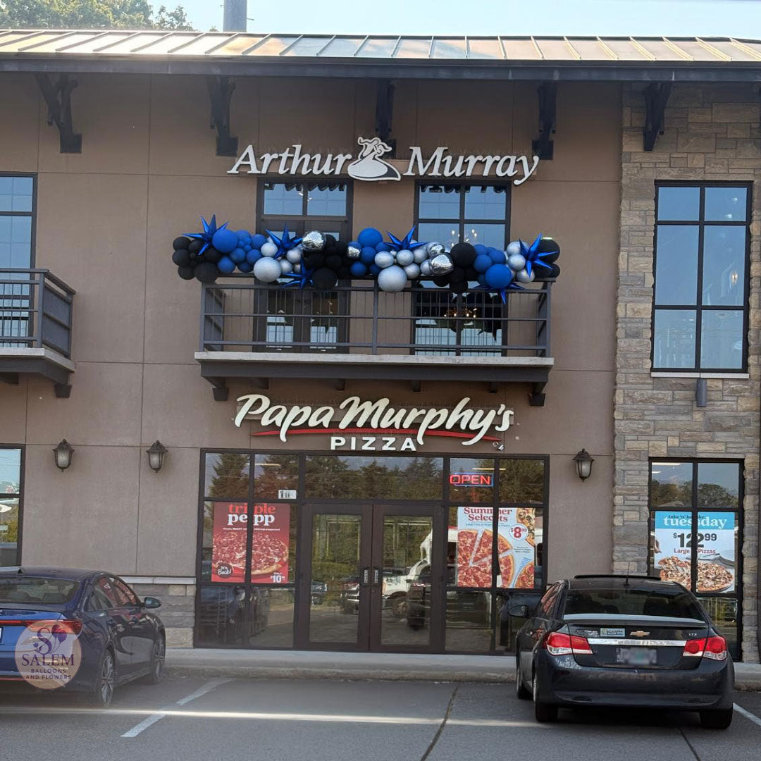 Front exterior of the Arthur Murray logo above the balcony, blue, black, and white balloon decorations attached to the balcony by Salem Balloons and flowers.