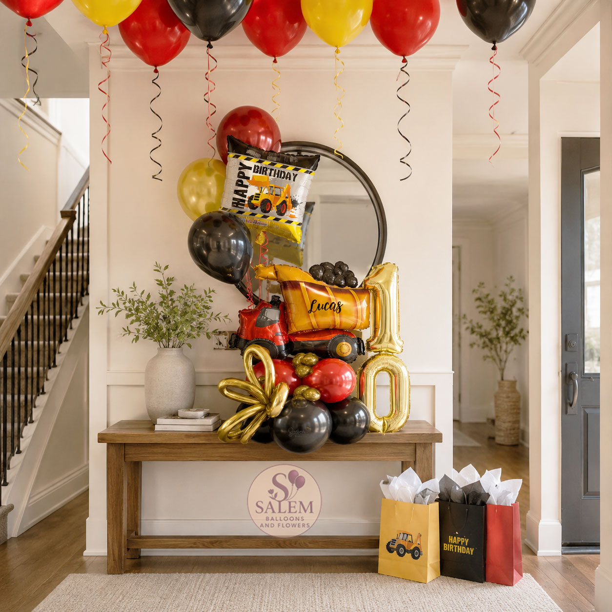 Decorative birthday setup with balloons, gift bags, and a mirror in a home interior, featuring a large balloon arrangement with a construction truck theme in red, yellow and black. Oregon balloon delivery.