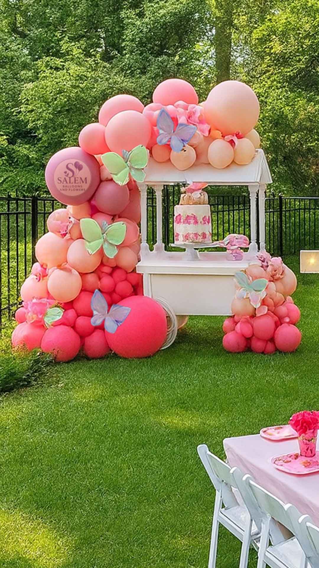 White candy cart decorated with a  balloon garland with pink and white theme in a garden setting. Balloon decoration plus candy cart rental. Oregon