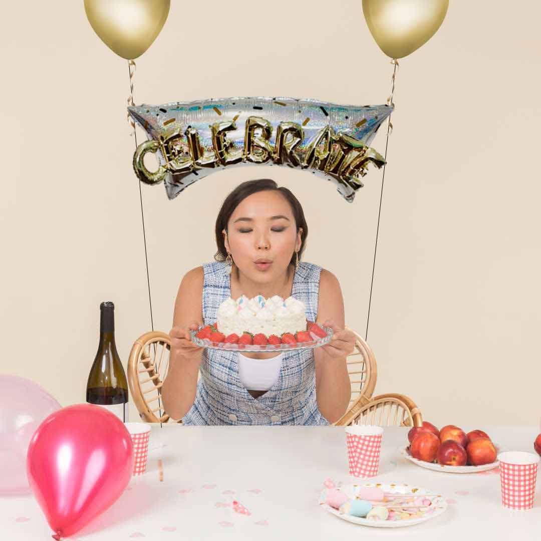 a girl blowing a cake candles with a Helium balloon bouquet tied to a chair in gold and silver with the word "Celebrate". Oregon balloon delivery