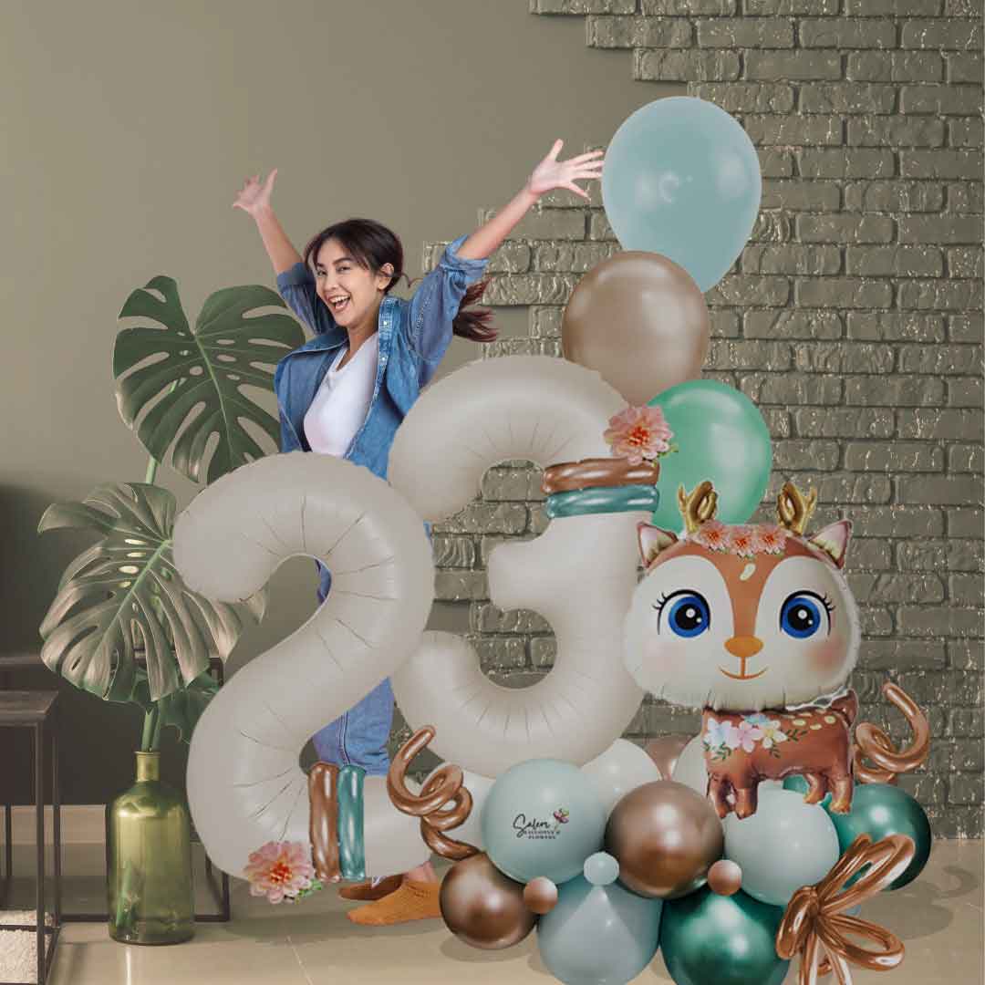 Young woman behind a Christmas themed balloon marquee with large balloon numbers and a balloon reindeer. Decorated with flowers and helium balloons. Balloon delivery in Salem Oregon and nearby cities.