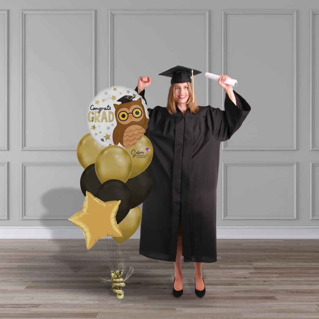 A grad standing next to a Graduation helium balloon bouquet. Congrats grad balloon bouquet. Featuring a Mylar balloon with a "Congrats grad" message with gold and black balloons. Delivery in Salem OR. and nearby cities.