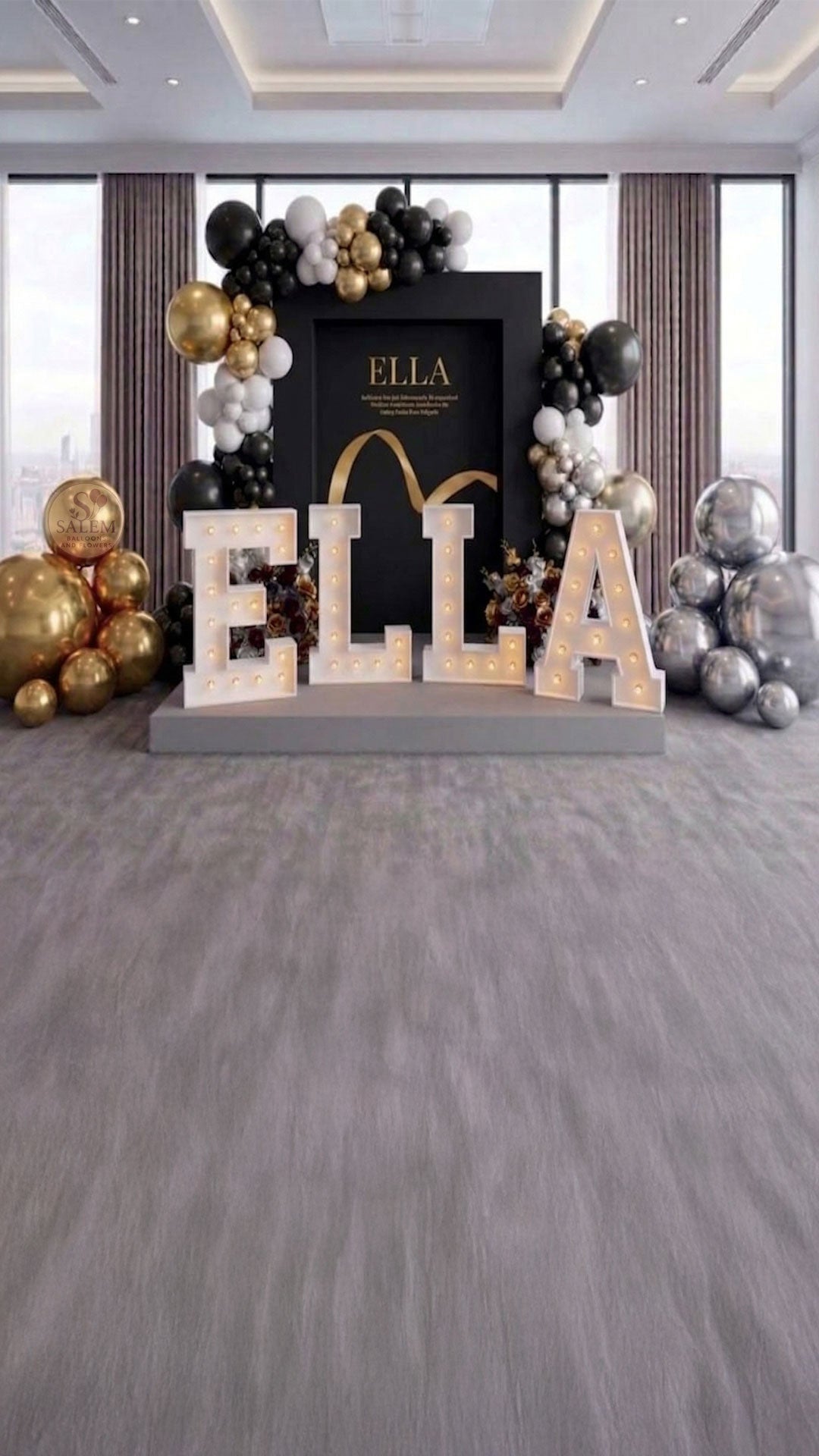 Decorative executive setup for a brand display with 'ELLA' letter lights and balloon garlands, on a platform in a venue room with large windows. Event decor. Oregon.