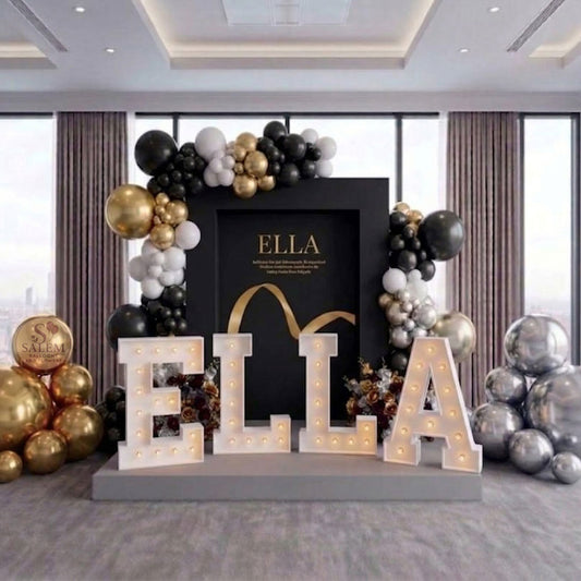 Decorative executive setup for a brand display with 'ELLA' letter lights and balloon garlands, on a platform in a venue room with large windows. Event decor. Oregon.