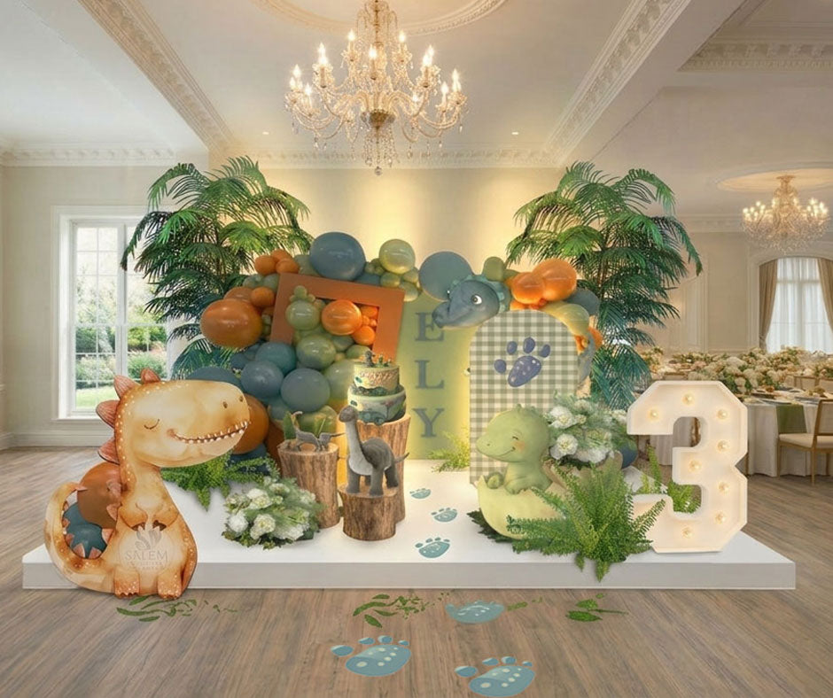 Dinosaur-themed birthday party setup with decorations in a green blue and orange color palette, decorated with greenery, palms, dinosaurs cutouts, marquee number 3 in an elegant venue room with chandeliers. Balloon Decor Oregon.