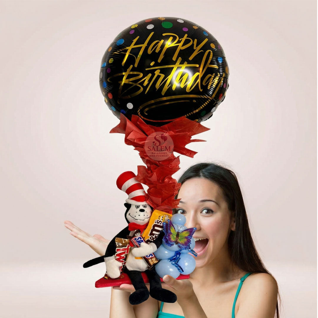 A balloon arrangement with a Dr. Seuss plush holding a Happy Birthday balloon and candy. Decorated with tissue paper. Salem Oregon balloon delivery.