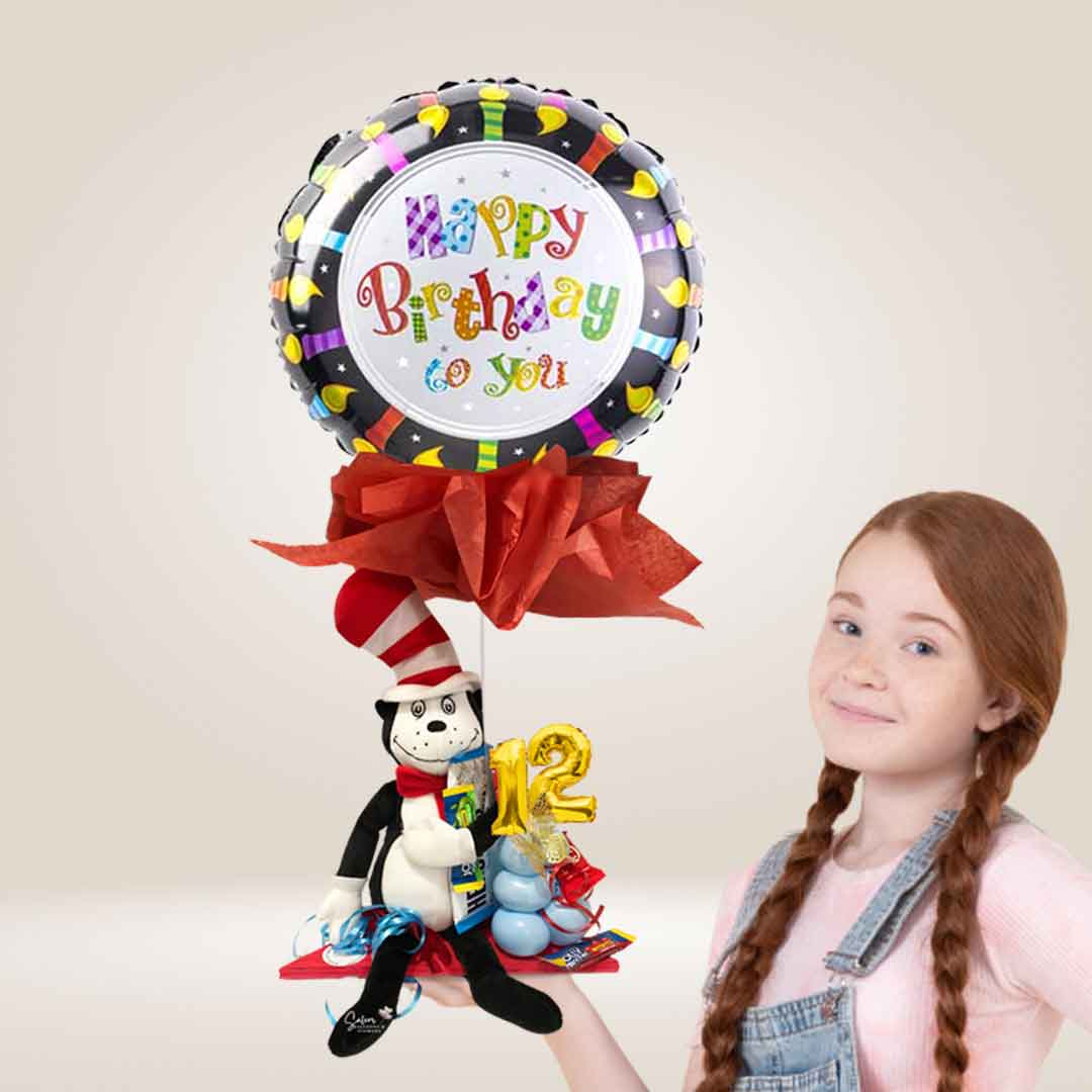 A girl holding a balloon bouquet with a Dr. Seuss plush holding a Happy Birthday balloon, candy and balloon numbers. Decorated with tissue paper. Salem Oregon balloon delivery.