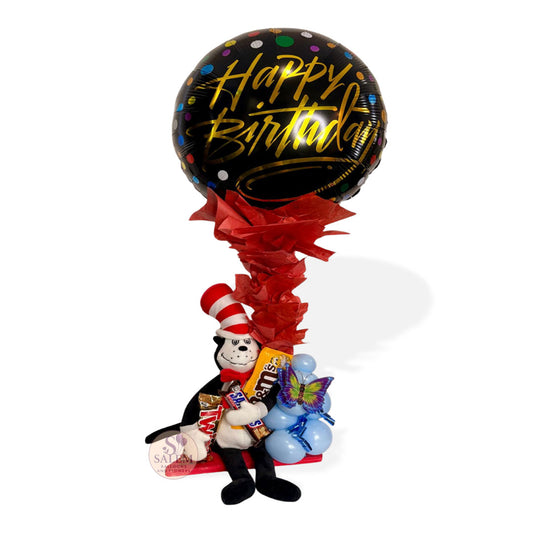 A balloon arrangement with a Dr. Seuss plush holding a Happy Birthday balloon and candy. Decorated with tissue paper. Salem Oregon balloon delivery.
