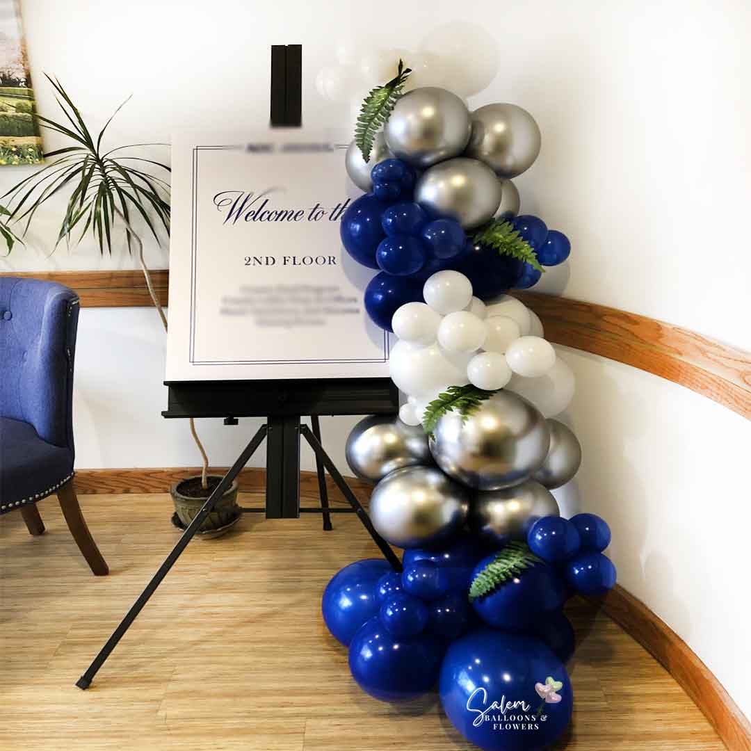 Balloon garland on an Easel in blue, white and silver colors and decorated with fern leaves. Salem Oregon Balloon decor. Balloon decorations.