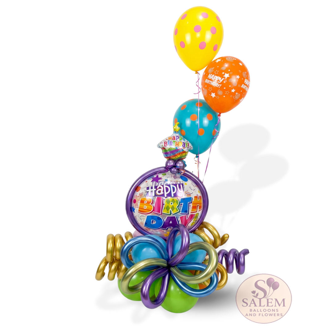Luxury colorful birthday balloon bouquet featuring a round 'Happy Birthday' focal balloon, decorative metallic twists, and vibrant helium balloons on a crisp white background with natural shadows. with a Salem Balloons and Flowers logo.