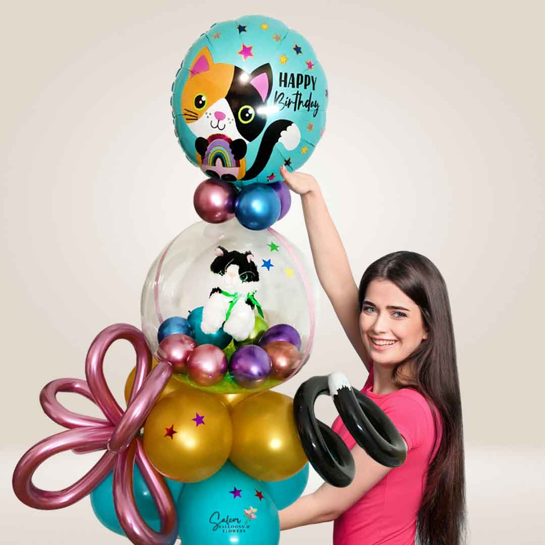 a girl holding a big Stuffed bubble balloon arrangement. Featuring a Kitty cat plush stuffed in a bubble balloon and a Mylar balloon with a "Happy Birthday" message. Salem Oregon balloon delivery.