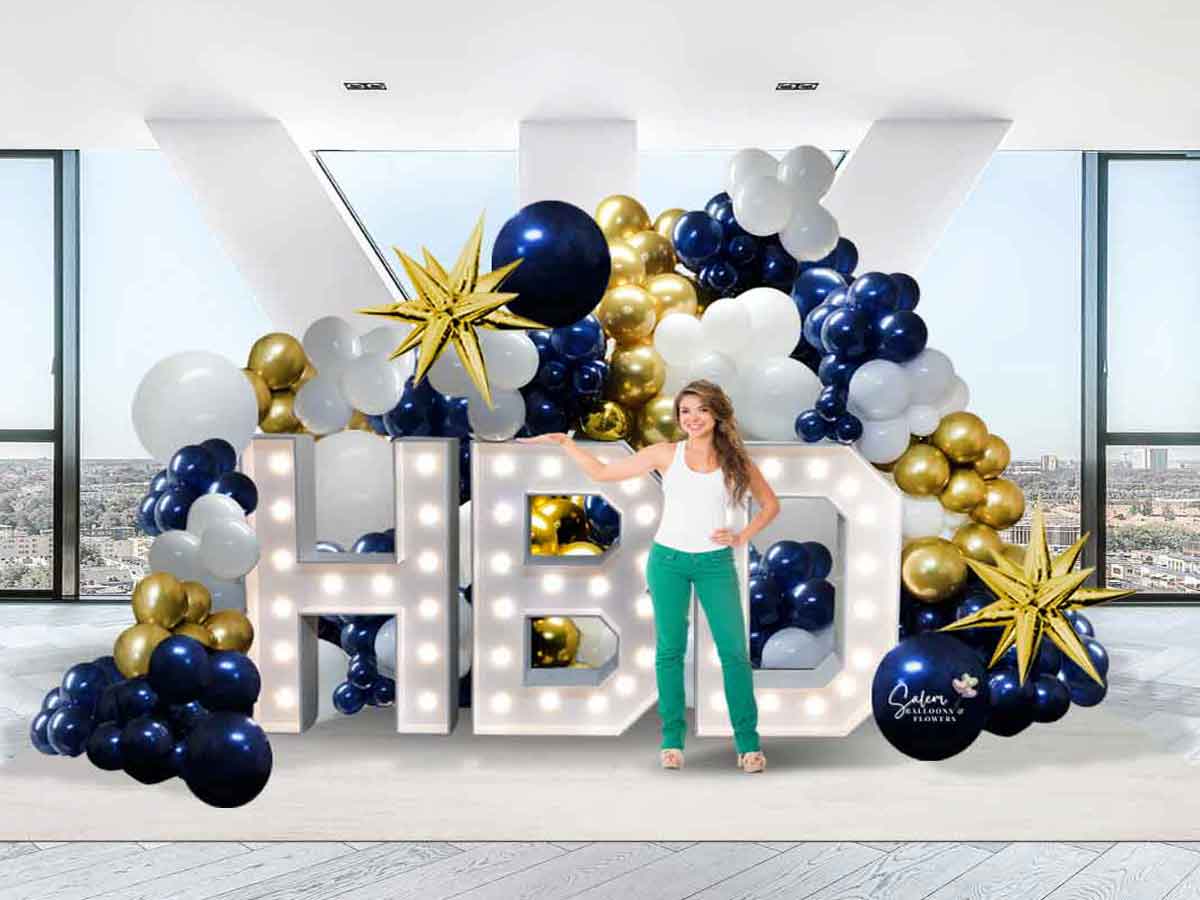 A young girl posing in front a balloon display with light-up marquee letters. Salem-Keizer Balloon decor