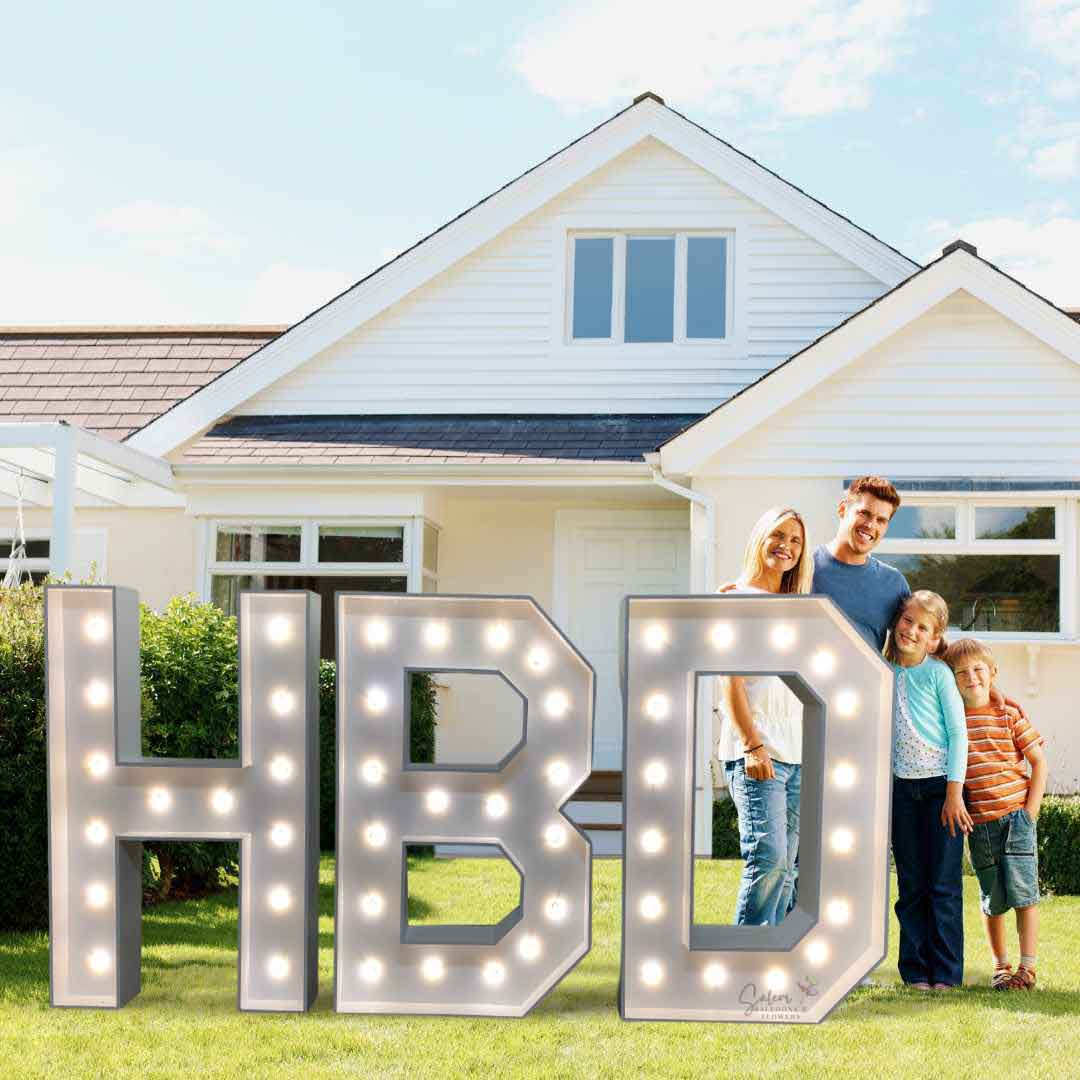 A family standing behind a white light-up HBD marquee letters in front of a house. Salem Oregon Balloon decor