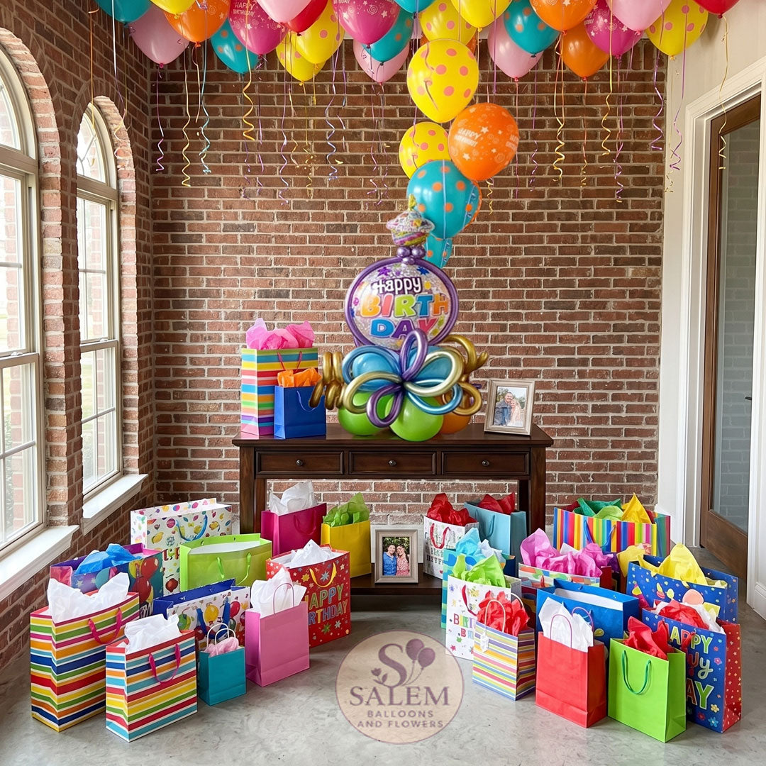 Birthday party setup with colorful balloons and gifts against a brick wall. With a Salem Balloon and Flowers logo.