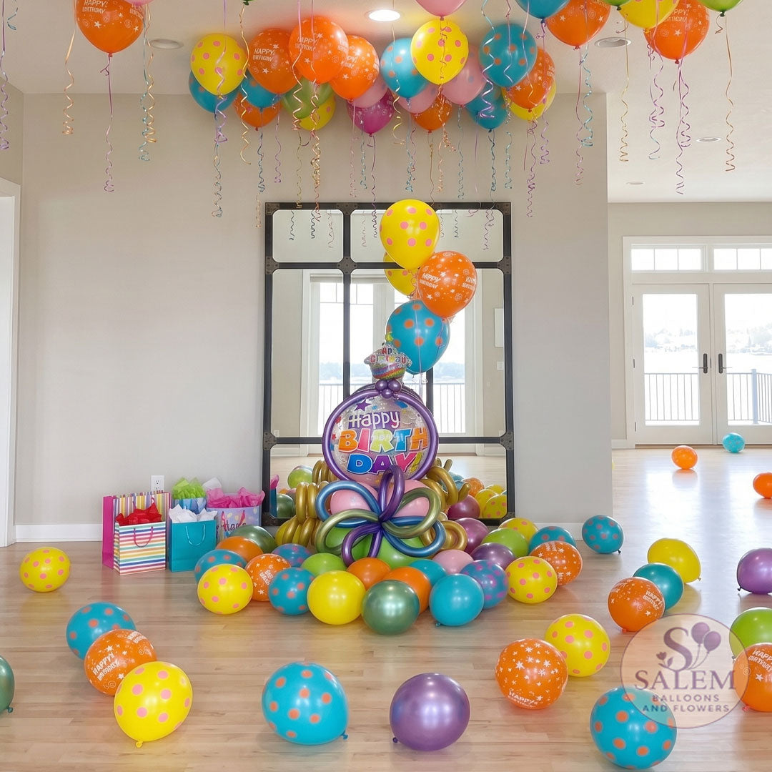 Festive birthday room decor installation featuring a colorful center balloon bouquet in front of a large mirror, with matching colorful helium balloons scattered across the ceiling and loose balloons spread out across the hardwood floor. Birthday Balloon delivery in Salem ORegon and nearby cities.