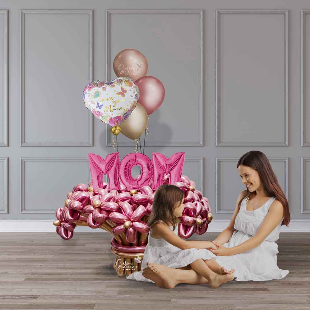 A mom and a daughter sitting next to a Mother's Day Flower balloon bouquet in various hues of pink and rose gold, with a MOM balloon sign and an I love you Mom message. Salem Oregon balloon delivery.