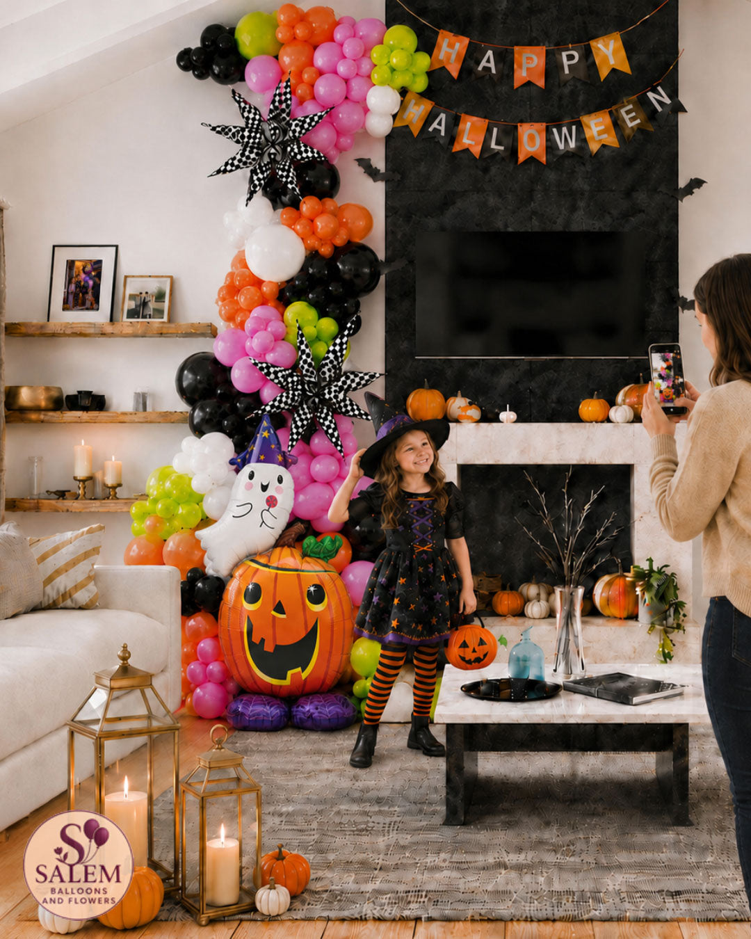 Girl in a witch costume posing beside colorful Halloween balloon décor while her mother takes a photo in a decorated Salem, Oregon home.