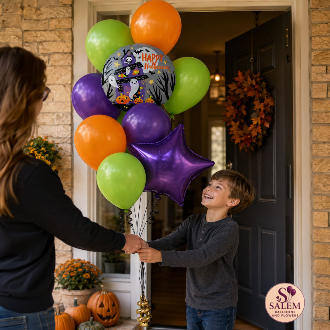 A delivery lady and a young boy stand at a front porch doorway holding a large balloon bouquet. The balloons are mostly orange, green, and purple, with one round foil balloon printed with a Halloween scene and the words “Happy Halloween,” plus a metallic purple star-shaped balloon with a Salem Balloons and Flowers logo at the bottom right corner.