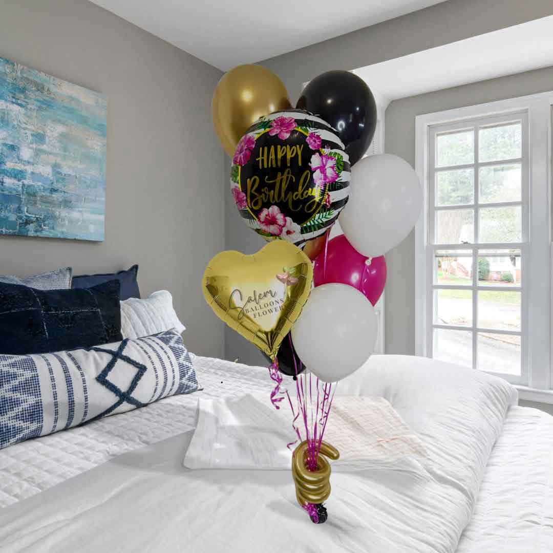 Hawaiian flower themed, Bouquet of colorful balloons with 'Happy Birthday' on a bed in a bedroom. Oregon balloon delivery.