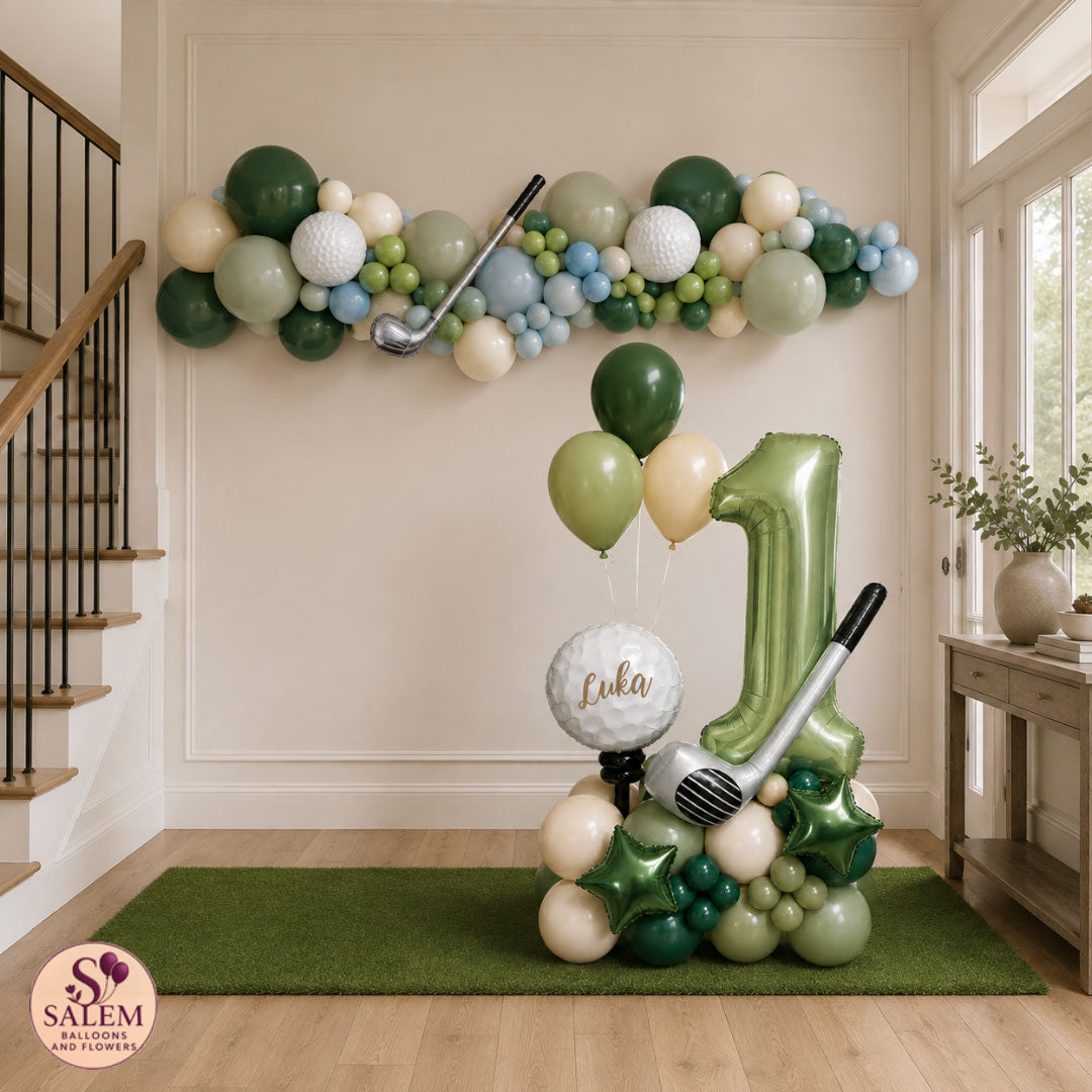 Golf-themed first birthday party decoration set in a home entryway, featuring a green number 1 balloon, a golf ball balloon with the name 'Luka', a golf club balloon, and a green balloon garland on the wall. With a Salem Balloons and Flowers logo on the left bottom corner.