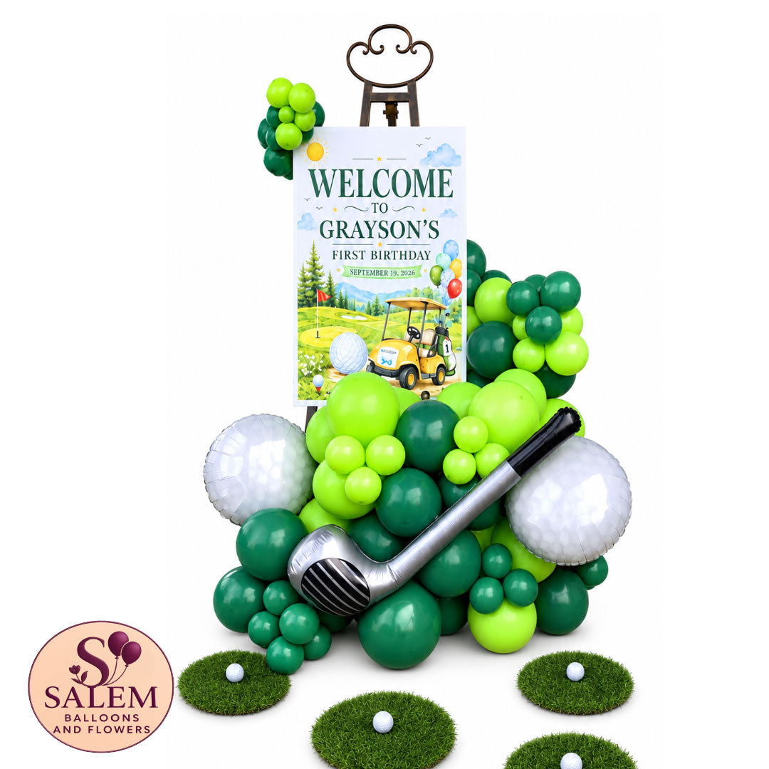 Hole in one. Golf themed balloon garland on an easel with round grass patches a golf club, and golf ball balloons on a white background with a Salem Balloons and Flowers logo.