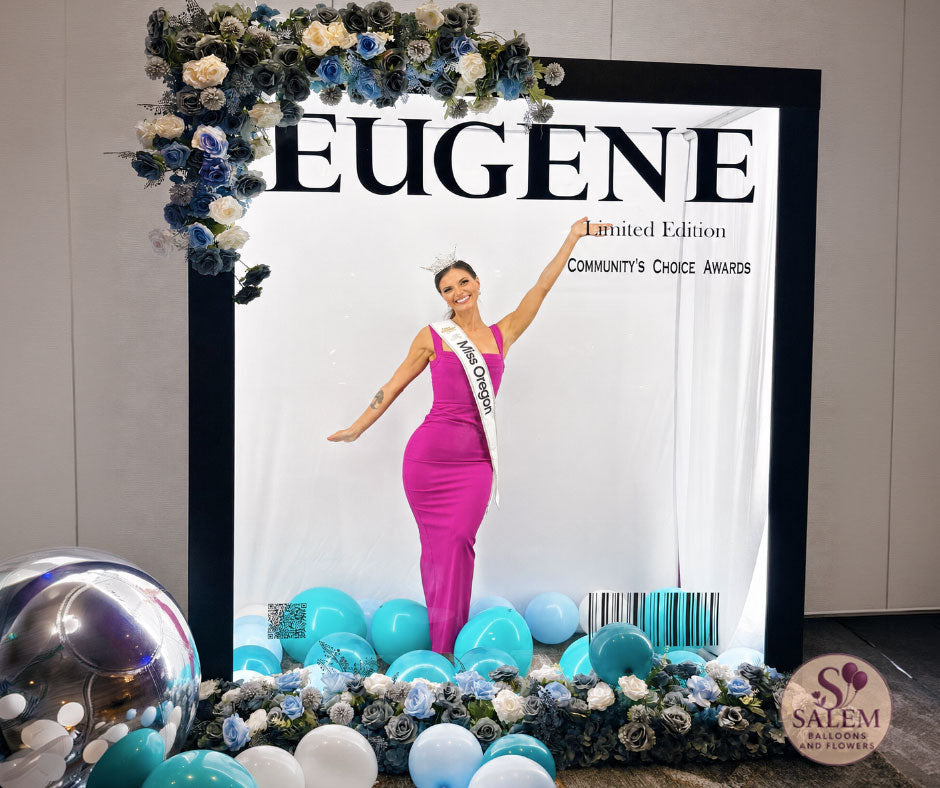Magazine photo booth decorated with flowers with a banners spelling: Eugene, Community's choice awards at The Graduate Hotel, Limited Edition and Miss Oregon posing inside for pictures. By Salem Balloons and Flowers. 