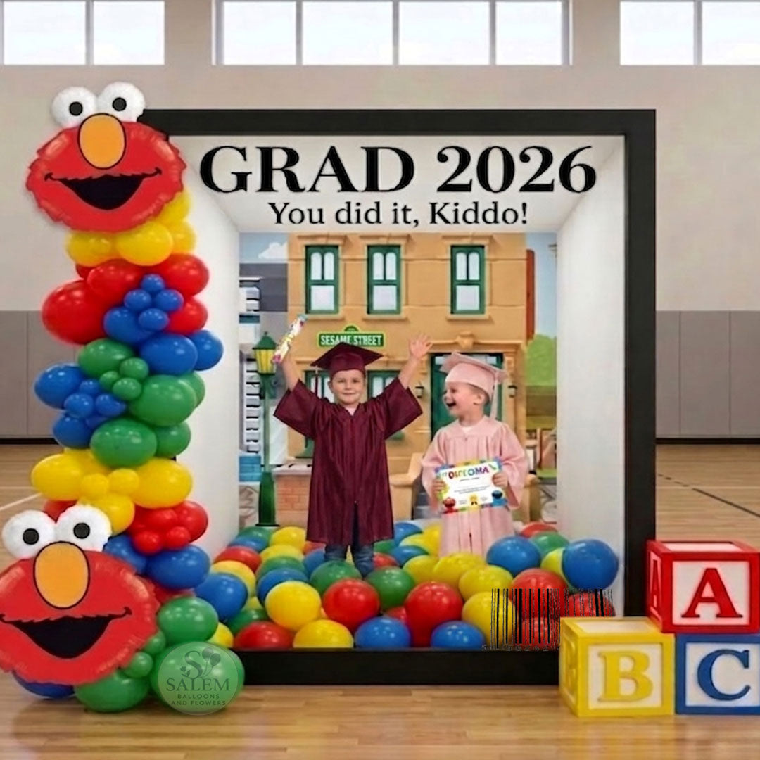 Graduation-themed magazine photo booth setup with colorful balloons and Sesame Street character Elmo in a school gym setting. Balloon decor. Oregon.