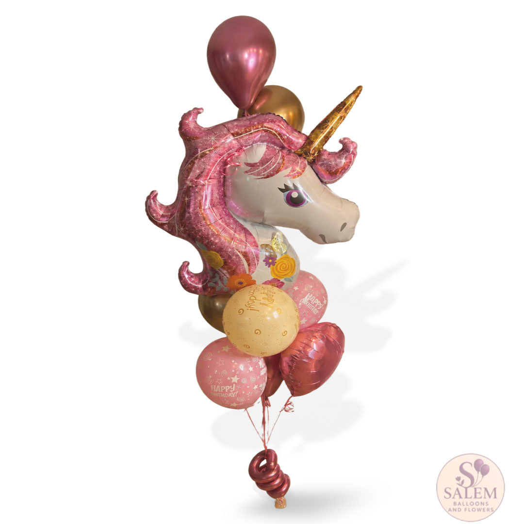 A decorative balloon bouquet featuring a large pink unicorn head balloon with a gold horn, accompanied by several metallic pink, rose gold, and gold balloons on a white background delivered by Salem Balloons and Flowers