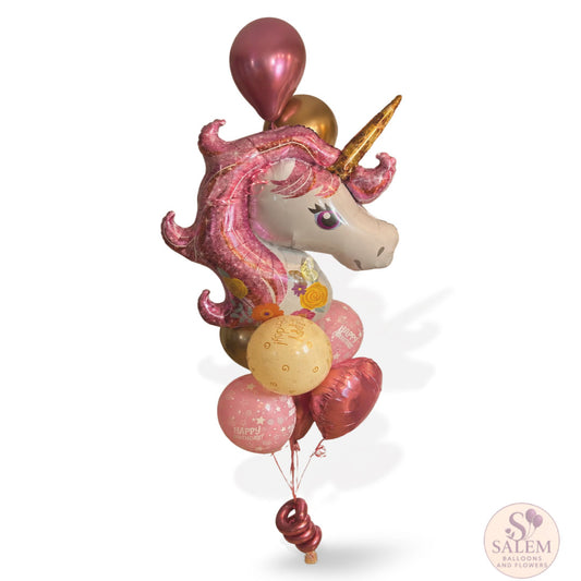 A decorative balloon bouquet featuring a large pink unicorn head balloon with a gold horn, accompanied by several metallic pink, rose gold, and gold balloons on a white background delivered by Salem Balloons and Flowers