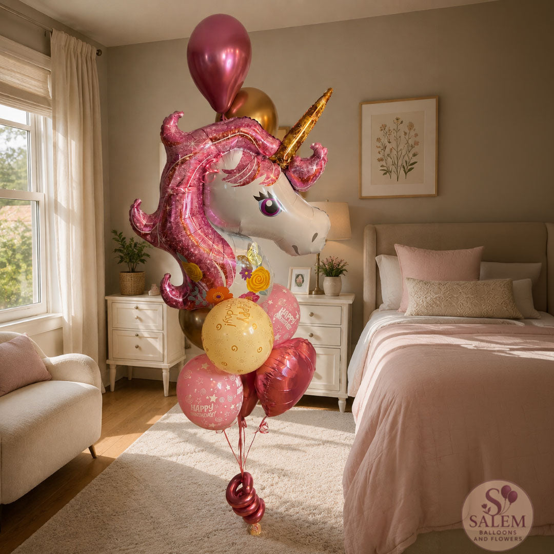 A large balloon bouquet with a large foil balloon shaped like a pink unicorn with a gold horn, accompanied by pink, gold, and pink chrome balloons, displayed in a beautifully decorated pink bedroom delivered by Salem Balloons and Flowers.
