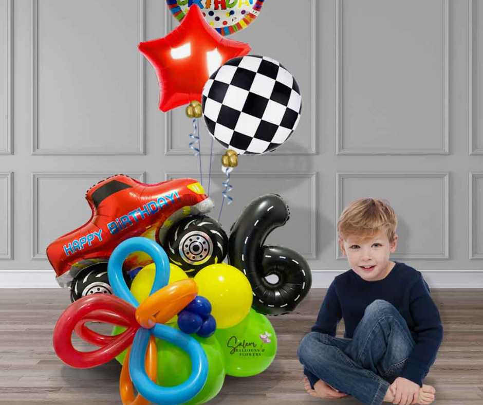Boy sitting next to a colorful Monster truck themed balloon bouquet with number 6. Salem Oregon Balloon delivery and balloon decor
