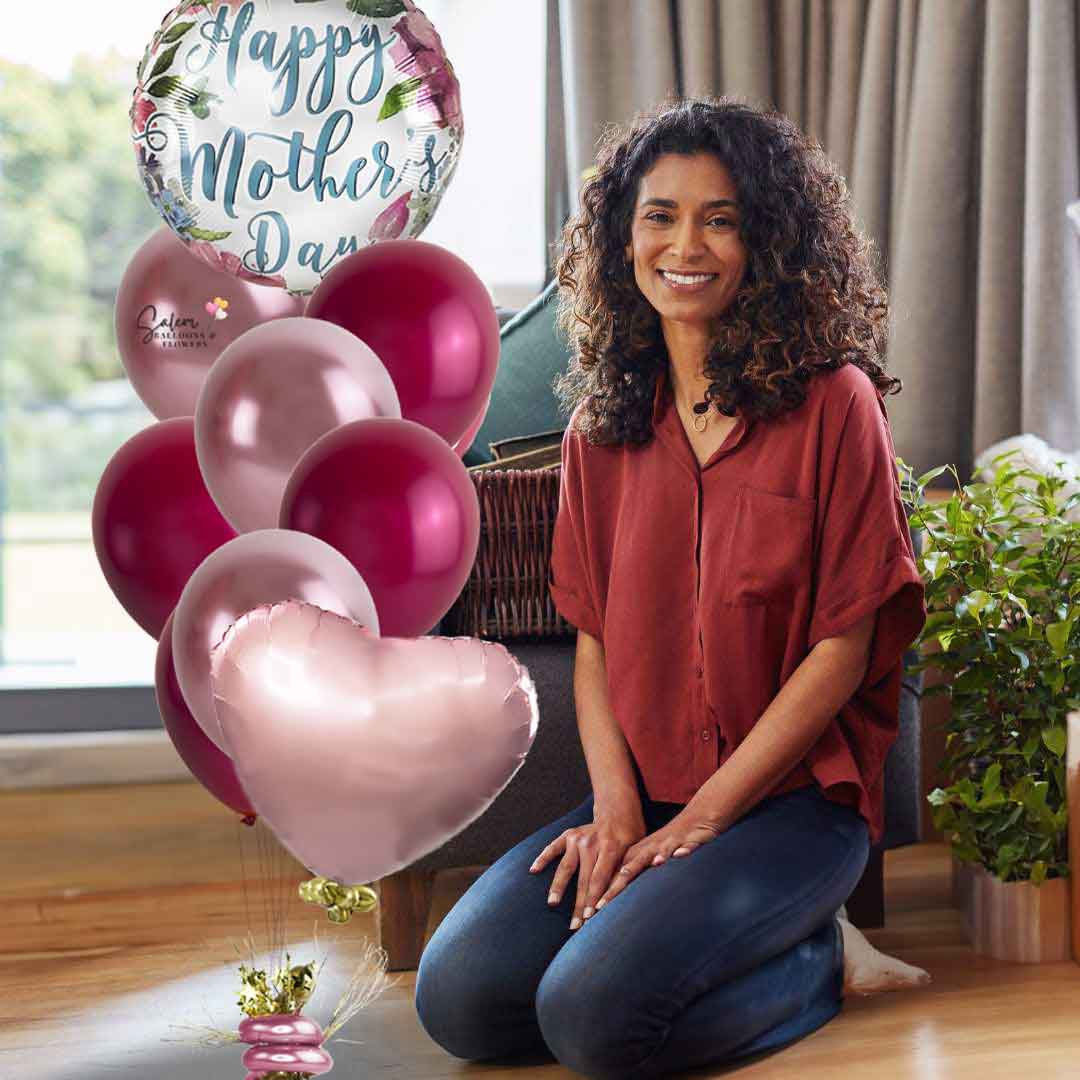 A mom kneeling next to a Mother's Day balloon bouquet, featuring a Mylar balloon with peony flowers and a 