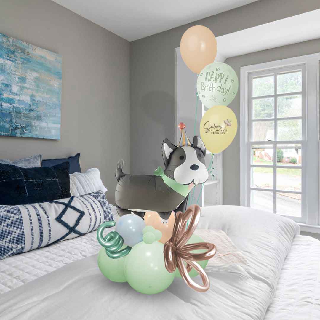 A Birthday Balloon Bouquet in pastel colors, featuring a gray dog balloon with white ears and decorated with curly balloons, standing on a bed. Oregon Balloon delivery.