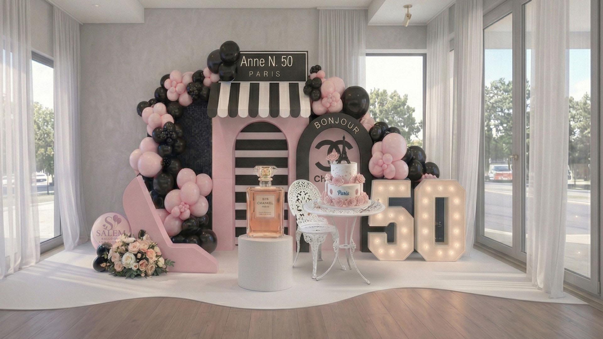 Decorative Parisian themed balloon decor setup with balloon garlands, a cake on a bistro paris style table, and '50' lights in a venue room. Balloon decor. Oregon.