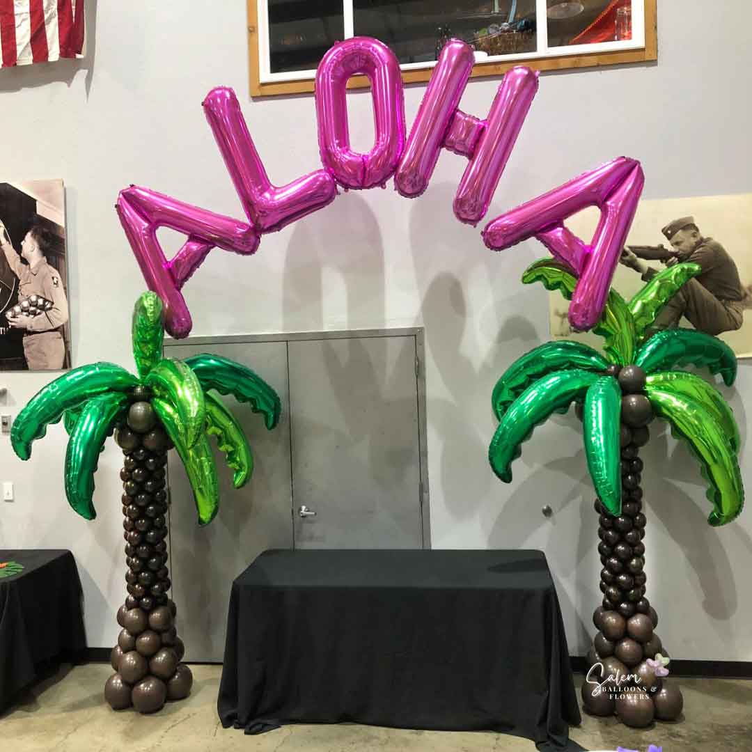 2 palm balloon columns with a pink ALOHA sign floating between them in a venue. Oregon Balloon Decor.