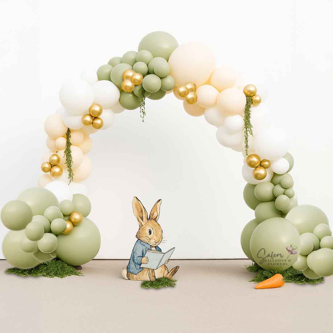 Balloon arch with green, white, and gold balloons, featuring a Peter Rabbit figurine and carrot on a white background. Balloon decor. Oregon