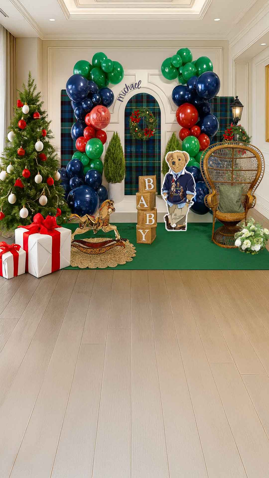 Decorative setup with balloon garlands in navy blue, red, and green, a Christmas tree, and teddy bear cutout, tall peacock chair and a rocking horse in a room. Baby shower balloon decor. Oregon.