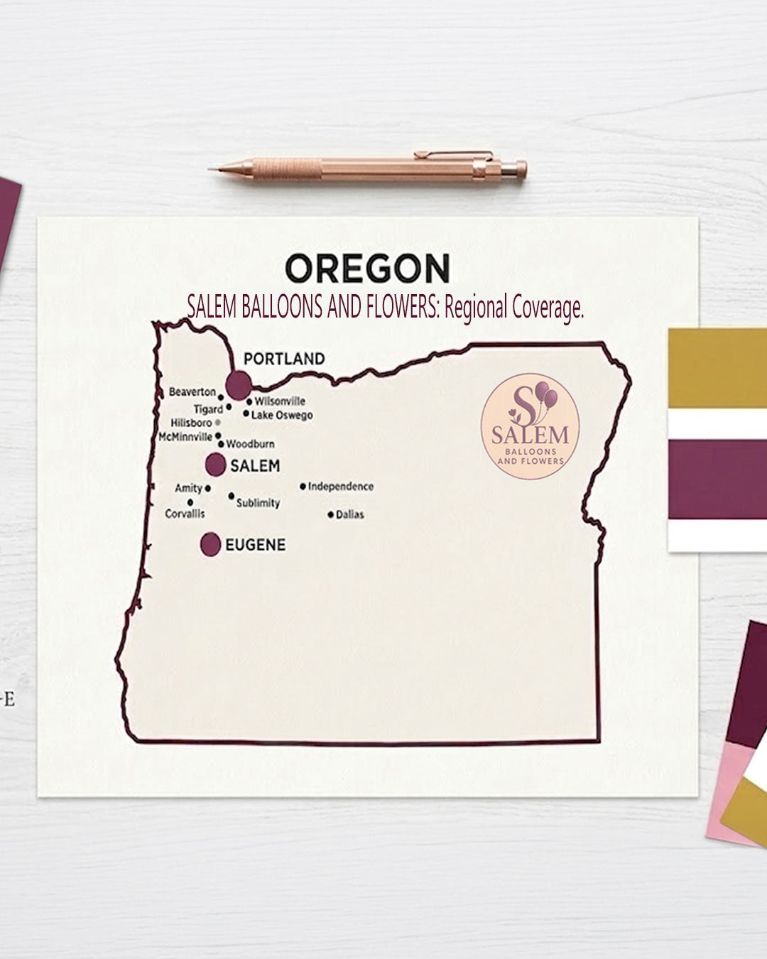 A professional service area map for Salem Balloons and Flowers, an Oregon event design studio. The minimalist map features a deep plum border and highlights primary service hubs in Salem, Portland, and Eugene with large branded markers. Surrounding cities including Lake Oswego, Beaverton, and Corvallis are noted with smaller markers, displayed on a bright, editorial-style designer's desk with rose gold drafting tools.
