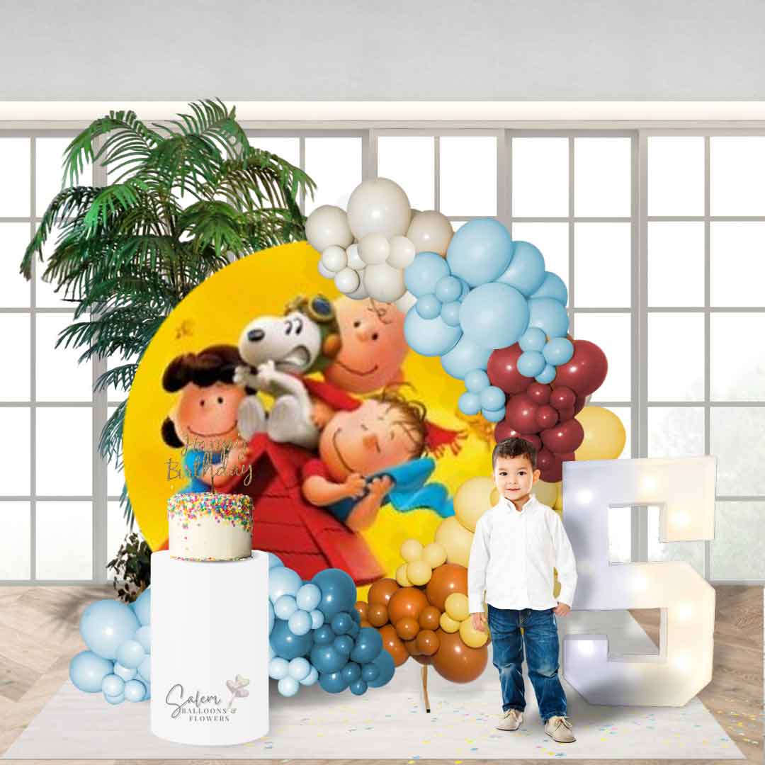 A boy posing for a picture in front of Balloon garland on a hoop frame with a Charlie Brown and Snoopy backdrop. Decorated with light up marquee numbers, cake pedestal and plants. Salem Oregon Balloon decor. Balloon decorations